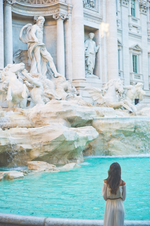 Beautiful woman in white dress sitting in front of Trevi Fountain, Rome, Italy. Happy woman enjoy italian vacation. Holiday in Europe.の写真素材