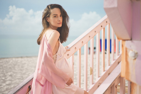 Outdoor atmospheric lifestyle portrait of beautiful pregnant woman in pink dress on pink lifeguard tower. Beautiful morning. Sunrise on the beach. Beauty and fashion. Pink aestheticの写真素材