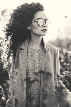 Outdoor fashion photo of young beautiful lady in autumn landscape with dry flowers. Gray coat, knitted sweater, sunglusses, wine lipstick. Fashion lookbook. Warm Autumn. Warm Springの写真素材