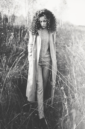 Outdoor fashion photo of young beautiful lady in autumn landscape with dry flowers. Gray coat, knitted sweater, wine lipstick. Fashion lookbook. Warm Autumn. Warm Springの写真素材