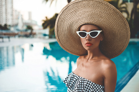 Lifestyle portrait of beautiful woman in straw hat in swimming pool. Summer resort. Beauty and healthの写真素材