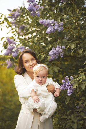 Outdoor fashion portrait of young beautiful mother and little cute daughter in blossoming park. Lilac blossom. Spring imageの写真素材