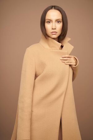 Fashion studio photo of young beautiful lady in beige coat on beige background. Total beige. Fashion look book. Warm Autumn. Warm Springの写真素材