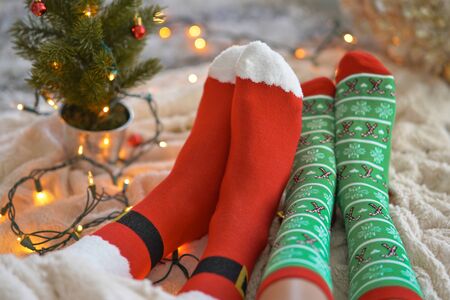 Feet in christmas socks near the Christmas tree. Couple sitting at the blanket, relaxes warming up their feet in woollen socks. Winter and Christmas holidays conceptの写真素材