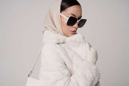 Beautiful young lady in a stylish white outfit. Refined taste. elegance. old money style. White faux fur coatの写真素材