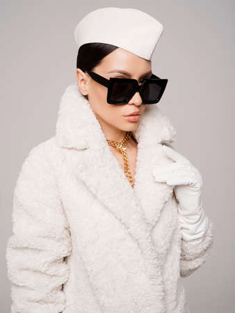Beautiful young lady in a stylish white outfit. Refined taste. elegance. old money style. White faux fur coatの写真素材