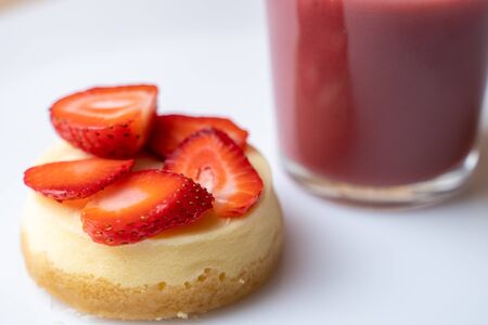 A slice of strawberry cheesecake with a nice raspberry drink in a glass on a white tableの写真素材