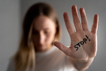 Woman with bruises on her face showing stop sign, palm in focus