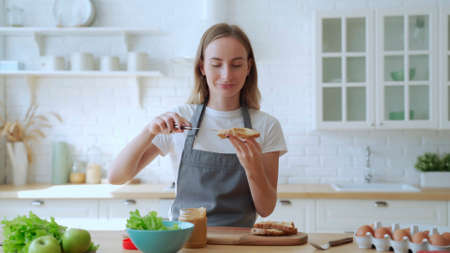 Happy smiling woman in the kitchen preparing a peanut butter sandwichの写真素材