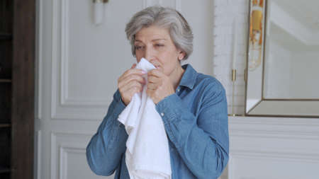 An elderly woman sniffs a fresh towel at home