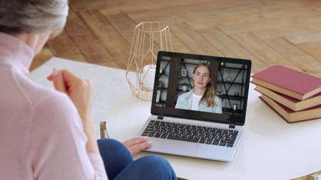 Over the shoulder view of an elderly woman video call a young daughter using a smartphone. The...