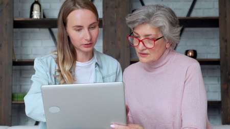 Happy two age generation of women. An older mother and an adult daughter have fun using a laptop at...