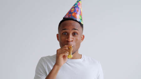 African man having fun at a party wearing a holiday hat while blowing a party hornの写真素材