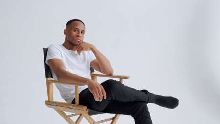 Dreamy athletic relaxed black young man sitting on a armchair against white wall backgroun