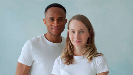 Young interracial couple stand in white t-shirts and smile at the cameraの写真素材