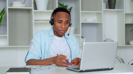 Focused black consultant with a headset looks at a laptop