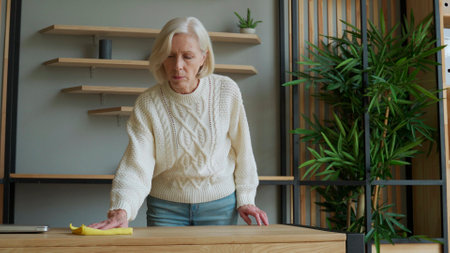 Elderly woman wipes her Desk with a rag. Concept of homework and household managementの写真素材
