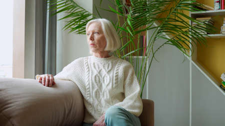 Old woman sitting in the chair and looking through the window.