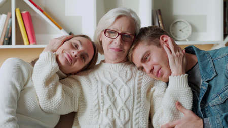 Smiling elderly mom hugging her daughter and son while sitting at home on the couch