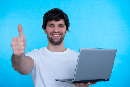Portrait of an excited man holding laptop computer and celebrating success isolated over blue...