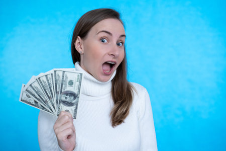 Banking savings. A young handsome confident woman is holding dollars in his hands happily looking at...