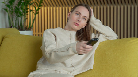 Woman is watching films by tv screen in her home, switches different channels with a remote sitting...