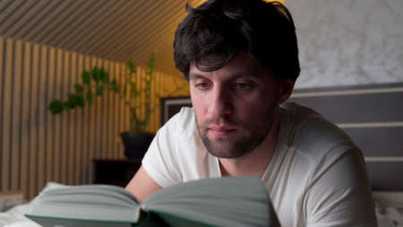 Man reads a book at home in the evening on the bed