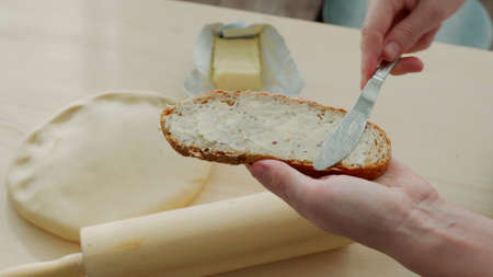 Spreading butter on bread. Hand holding piece of bread and smearing organic butter on itの写真素材