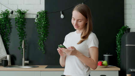 Smiling woman using smart phone in kitchen. Woman scroll through the social networkの写真素材