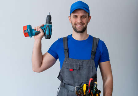 Uniformed maintenance worker holds a screwdriver and looks at the camera. Handyman wearing a tool...