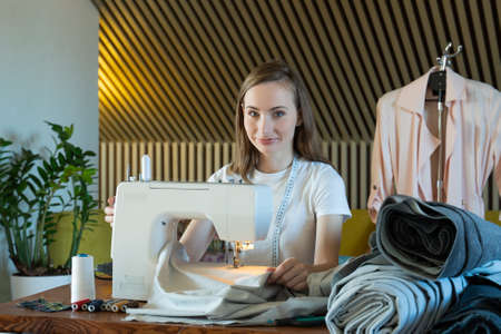 Young woman seamstress sews on a sewing machine sitting at a table