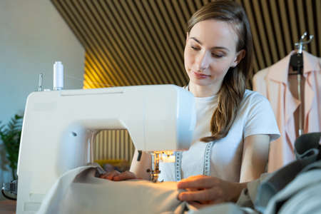 Woman seamstress sitting and sews on sewing machine. Sewing as small business conceptの写真素材