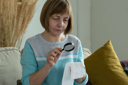 Woman looks at a receipt from a supermarket through a magnifying glass. Cost tracking and budgetingの写真素材
