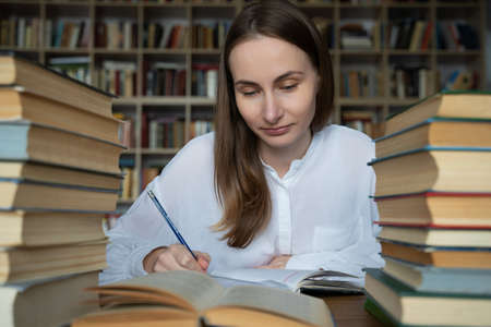 Female student sits at a table in the library, littered with books.