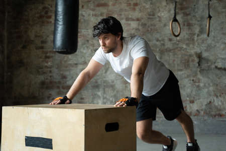 A man working out in the gym does push-ups from a wooden box