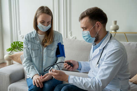 Doctor measures a womans blood pressure while sitting on the couch