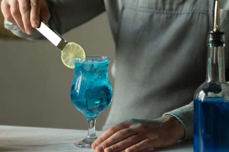 Bartender preparing at the bar counter Blue Lagoon cocktail. Man decorates a cocktail with limeの写真素材