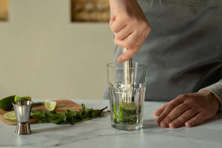 Bartender prepares a cocktail mojito using the madler. Bartender crushes mint and lime with a madler