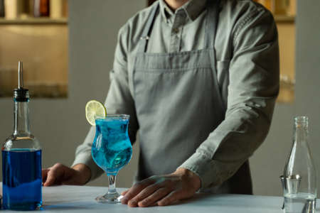 Blue Lagoon cocktail is on the bar, and a male bartender is standing next to itの写真素材