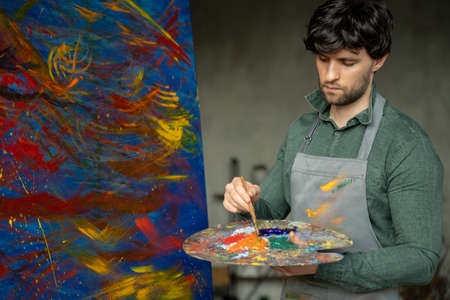 Man is an artist, holding a brush and drawing an abstract pictureの写真素材