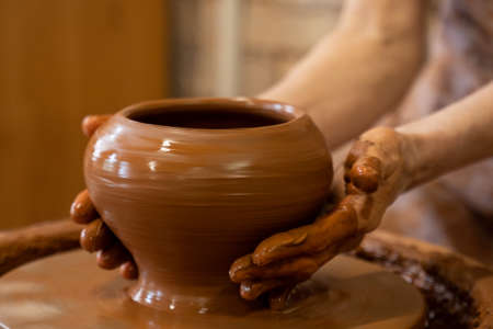 Old woman potter working on Potter wheel making a clay pot. Master forming the clay with her hands...