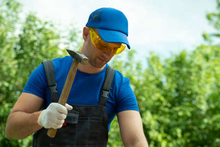 Carpenter hammers a nail into a wooden board while standing outsideの写真素材