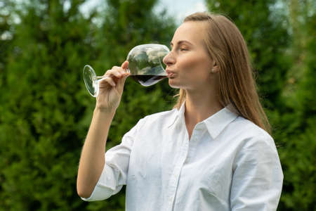 Young woman in a white shirt sniffs and tastes red wine on a green background