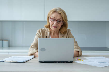 A smiling elderly woman using a laptop and looking at the camera. A business woman uses her laptop.