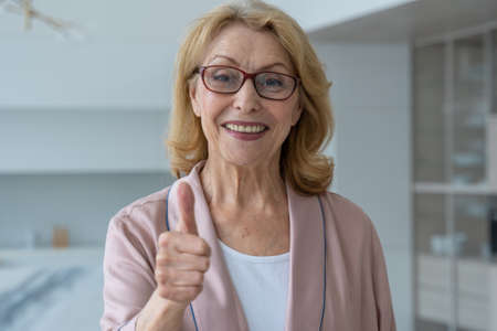 An elderly woman with glasses gives a thumbs up and looks at the camera