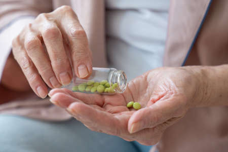 Womans hand is holding a medicine in close-up, an elderly woman is holding a pill in her hands,...