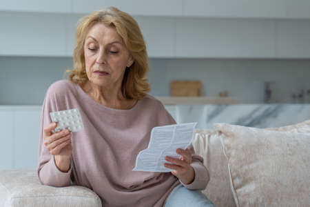 Elderly woman reads the instructions to the pills at home.の写真素材