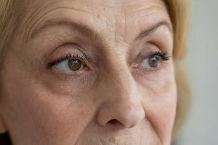 Sad brown eyes of an elderly woman looking away, taken close-upの写真素材