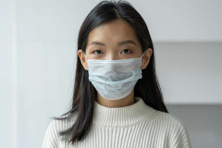Young Asian woman in a protective medical mask to protect against viral diseases looks into the camera. The concept of health, safety and pandemicの写真素材