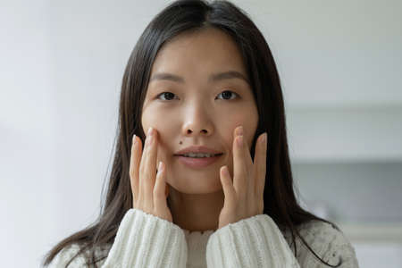 Beautiful woman touching her face by hands. Asian woman looking at the mirror with the trouble on her skin.の写真素材